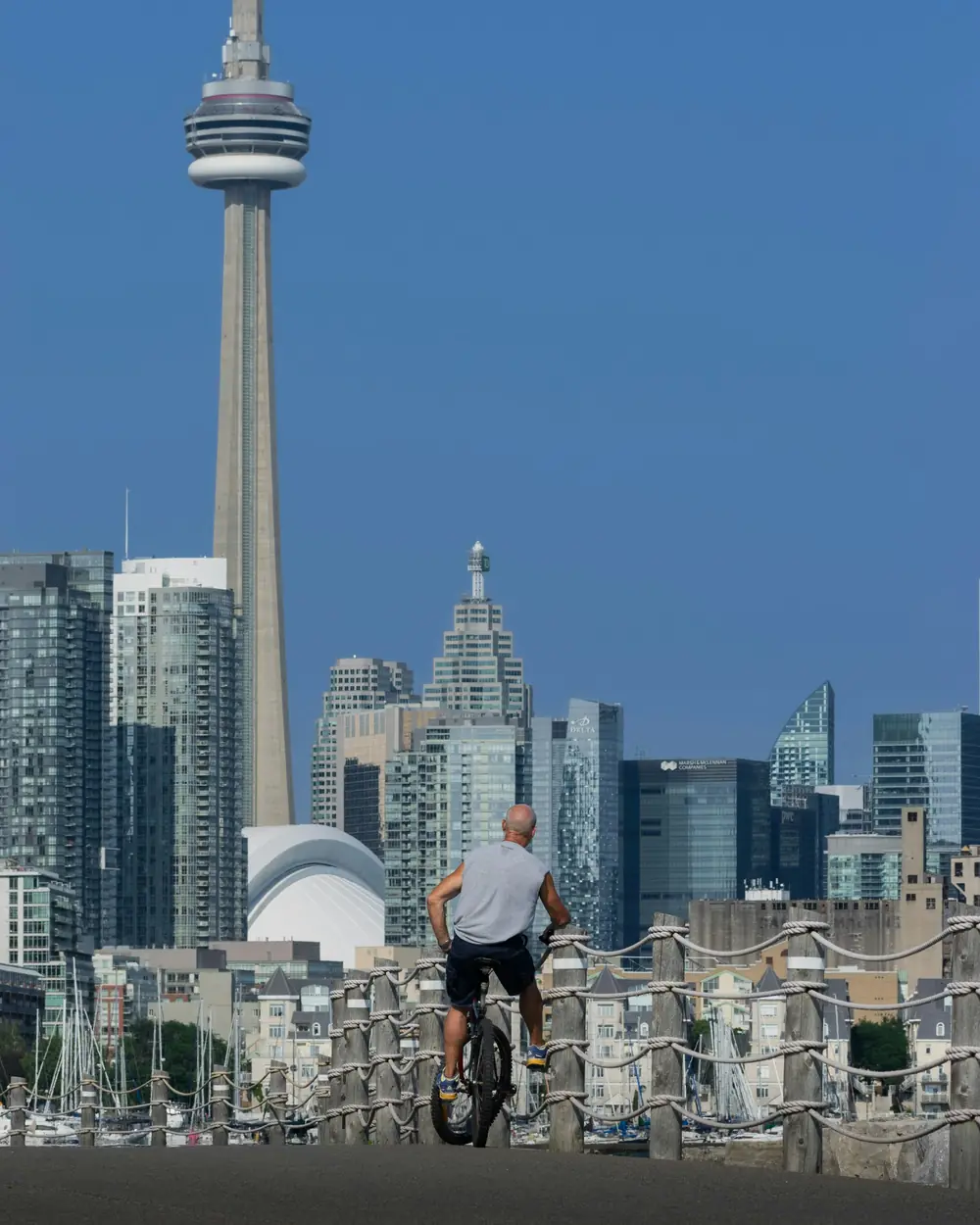 A cyclist stopped on the path at Ontario Place, looking out at the CN Tower and the Toronto skyline